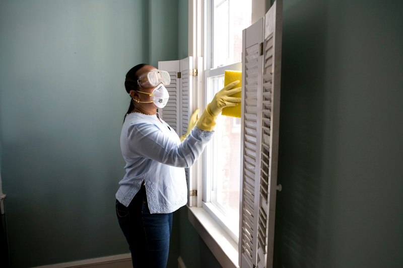 Technician in mask and gloves wiping a window frame during post renovation cleanup